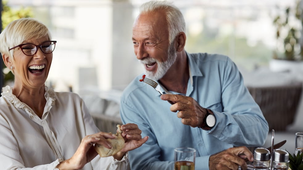 Senior man feeding woman breakfast and smiling.